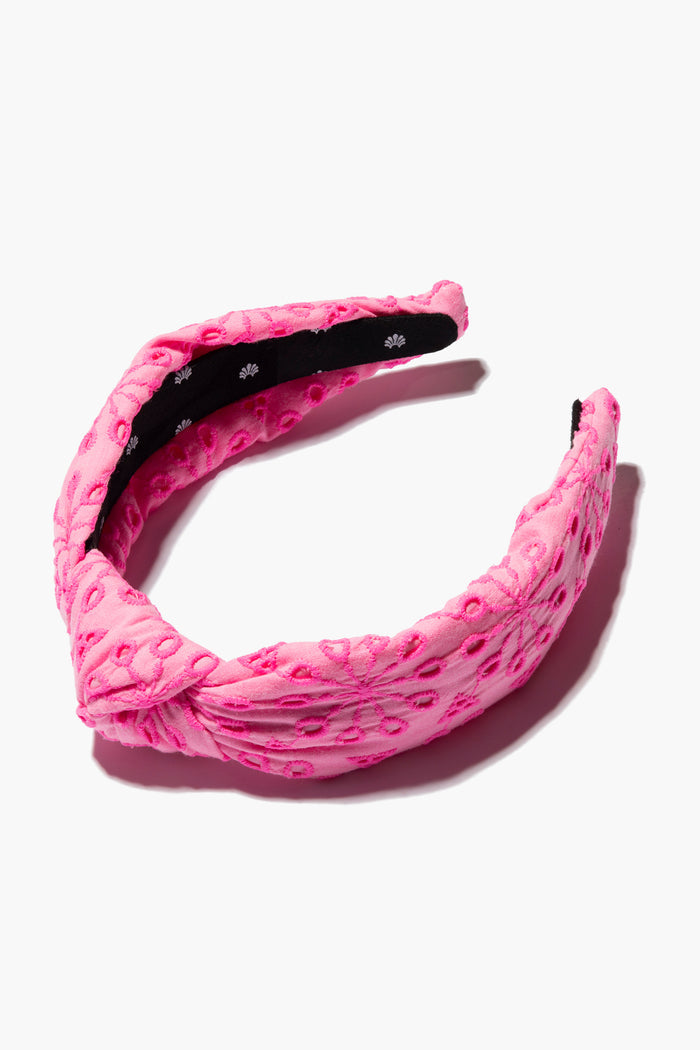A pink cotton eyelet headband by Lele Sadoughi, featuring an embossed floral pattern and twist knot detail, inspired by the Neon Sunburst Eyelet Knotted Headband from the Lilly Pulitzer collaboration.