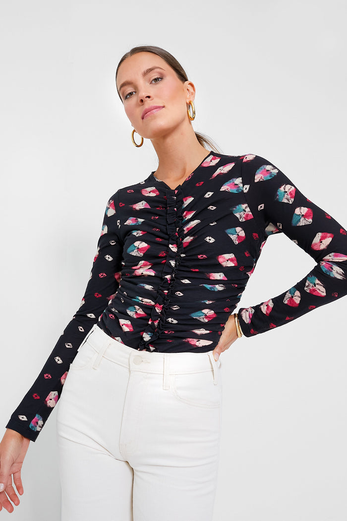 A woman wears an Ulla Johnson black floral ruched cotton jersey long-sleeve blouse with white high-waisted pants.