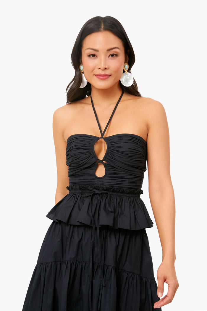 A woman wearing a black Ulla Johnson strapless dress featuring a ruched bodice, corset-style top, keyhole cutout, and ruffled skirt.