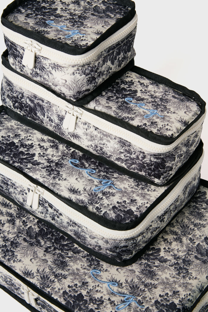 Set of four Tuckernuck Accessories packing cubes featuring black and white floral patterns, white zippers, and blue cursive embroidery—ideal for organizing travel essentials in your suitcase.