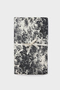 A folded black and white floral cotton Tuckernuck Home tablecloth, tied with a cream-colored ribbon, ready to use on your rectangle table.