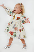A toddler in a Pink Chicken vintage floral baby girl dress and silver shoes stands with arms outstretched, gazing upward.