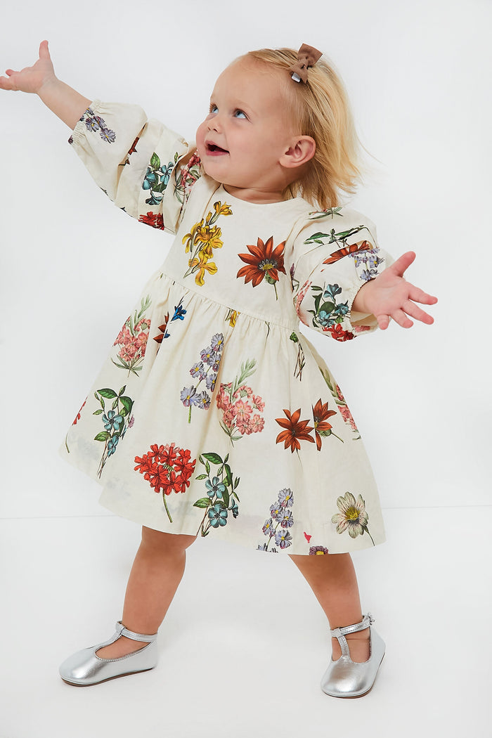 A toddler in a Pink Chicken vintage floral baby girl dress and silver shoes stands with arms outstretched, gazing upward.