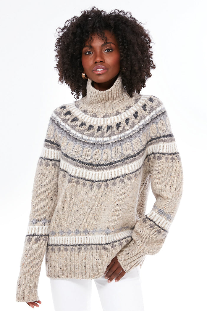 A person in an oatmeal combo apres ski turtleneck and white pants confidently showcases the Alex Mill beige and gray Donegal knit sweater featuring a cozy Fair Isle design.