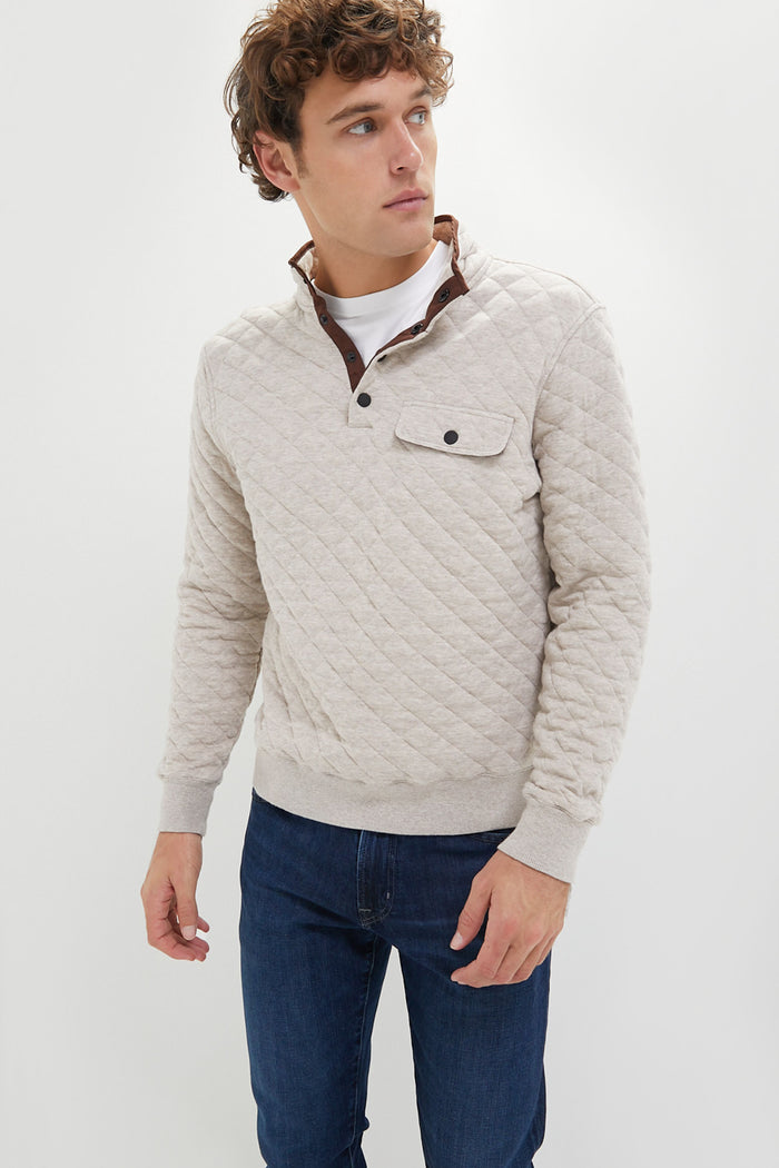 A man wears a light beige Faherty Epic Fleece Pullover with a chest pocket and blue jeans, highlighting this sustainable essential.