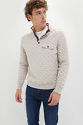 A man wears a light beige Faherty Epic Fleece Pullover with a chest pocket and blue jeans, highlighting this sustainable essential.