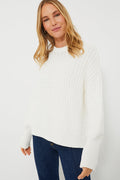 A woman models The Knotty Ones’ sustainable white long-sleeve knit sweater with blue jeans, highlighting elevated knitwear style.