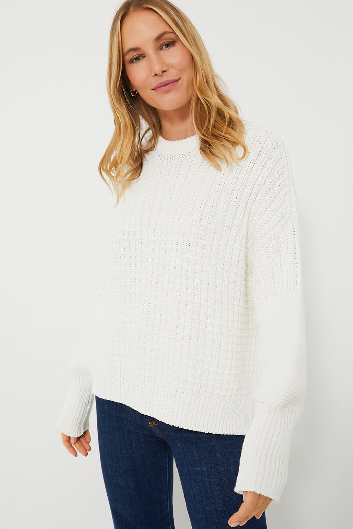 A woman models The Knotty Ones’ sustainable white long-sleeve knit sweater with blue jeans, highlighting elevated knitwear style.