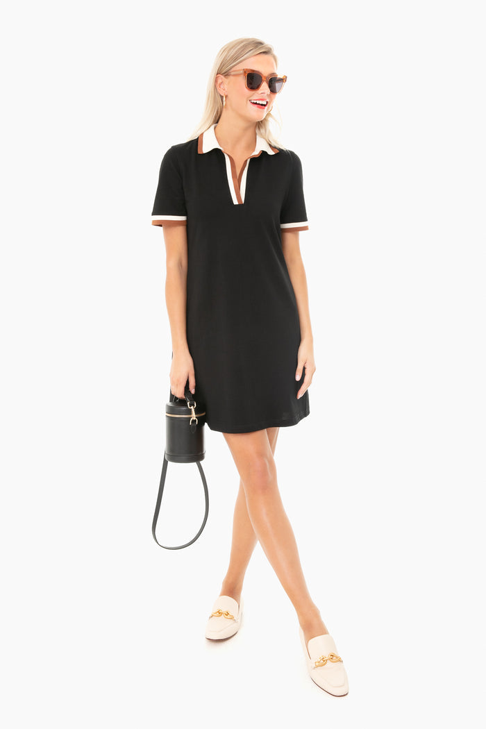 A woman in a Tuckernuck black short-sleeve polo tennis dress, light loafers, sunglasses, and carrying a small black handbag exudes sporty chic style.
