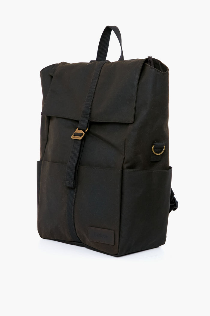 The Barbour black waxed canvas backpack features a flap closure, front strap, side pockets, gold-tone hardware, and adjustable webbed straps, drawing inspiration from the classic Olive Knapsack.