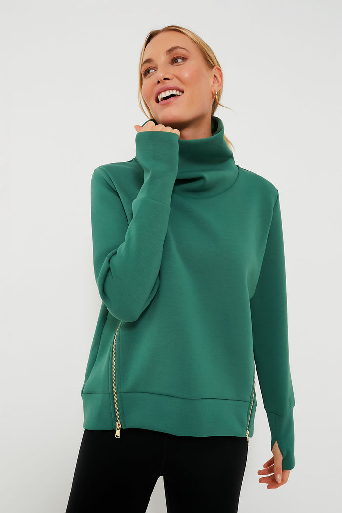 A woman stands confidently in an Addison Bay green turtleneck pullover with side zippers and black pants.