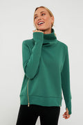A woman stands confidently in an Addison Bay green turtleneck pullover with side zippers and black pants.