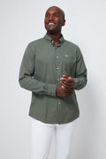A man stands smiling, wearing a tailored-fit Barbour Olive Grove green checkered shirt with white pants.