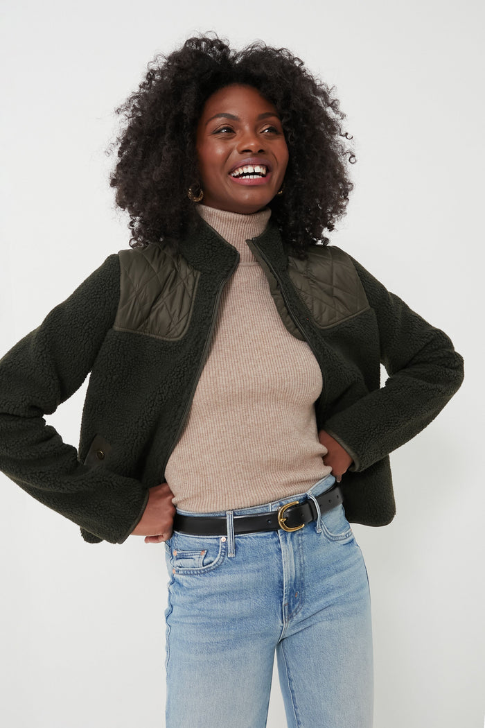 A woman smiling with hands on her hips, wearing a cozy Barbour sherpa jacket.