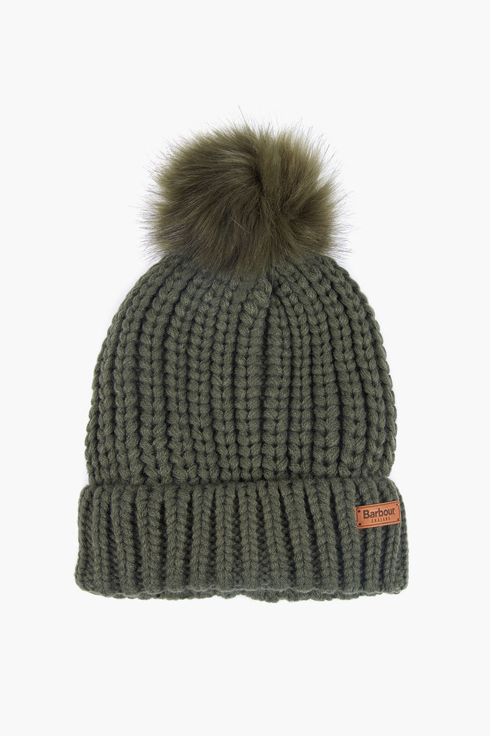 A Barbour olive green knitted winter beanie featuring a folded brim, brown brand label, and a large faux fur pom-pom on top.