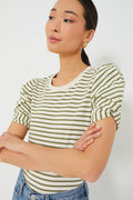 A woman stands with arms crossed, wearing a Pomander Place white and olive striped crewneck puff short sleeve top paired with blue jeans.