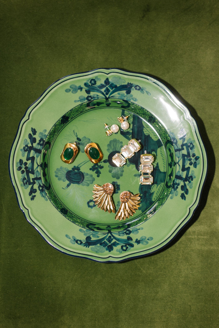 A Ginori 1735 Oriente Italiano Malachite green porcelain salad plate showcases six pairs of gold and gemstone earrings arranged elegantly on a green velvet surface.
