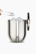 A Snowfox double-walled stainless steel ice bucket filled with ice cubes sits open, as tongs lift an ice cube above the insulated barware container.