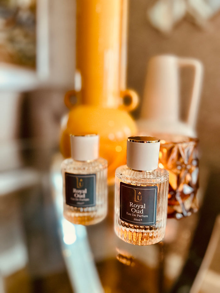 Oud & Bergamot Eau de Parfum by LU Fragrances — 50ml and 10ml bottles on a glass surface with warm amber and yellow home decor