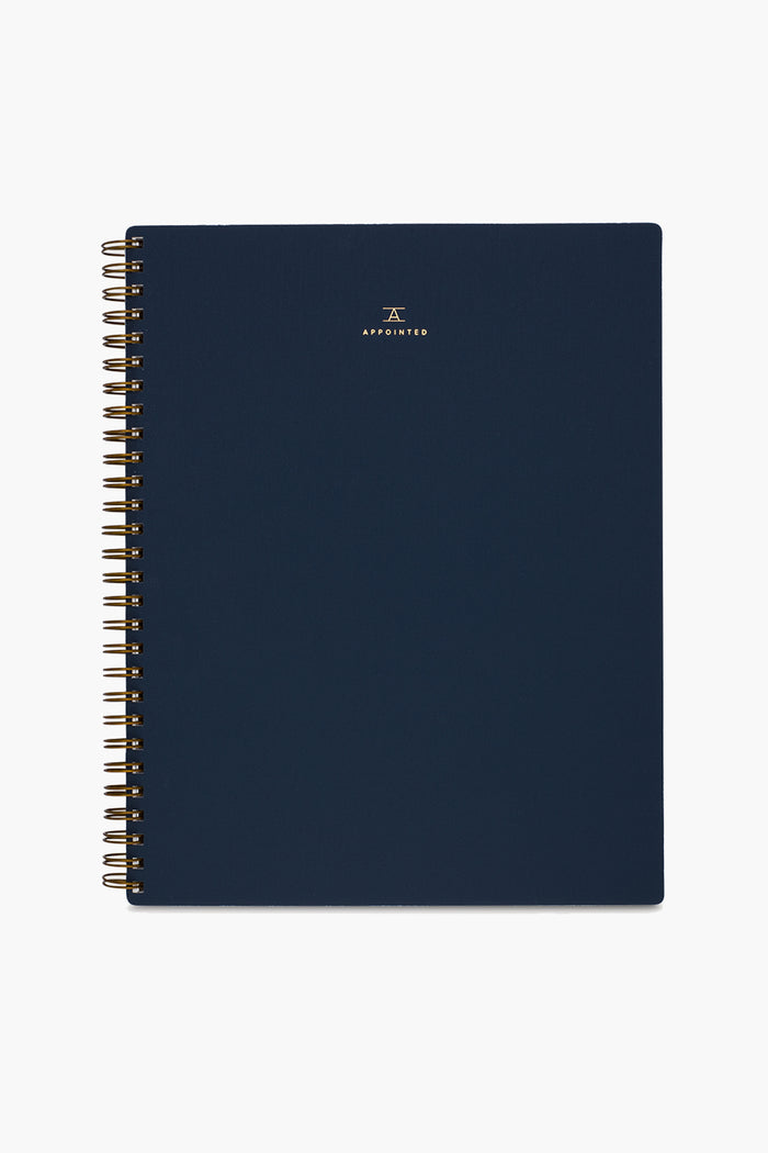 A navy blue spiral-bound APPOINTED Blue Lined Notebook with gold wire binding, a book-cloth cover, and a small gold logo and centered text on the front.