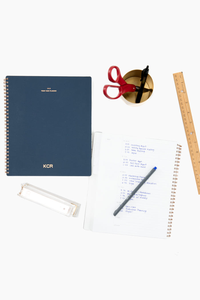 Classic desktop stationery flat-lay featuring the Oxford Blue Lined Notebook with a water-resistant cover, showcasing effortless style. Includes a weekly planner, brass cup, and clear stapler.
