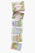 A LouLou Baker box with a pink and green leaf design sits above six Palm Beach playing cards, each with watercolor scenes or objects—making them perfect for unique gifts.