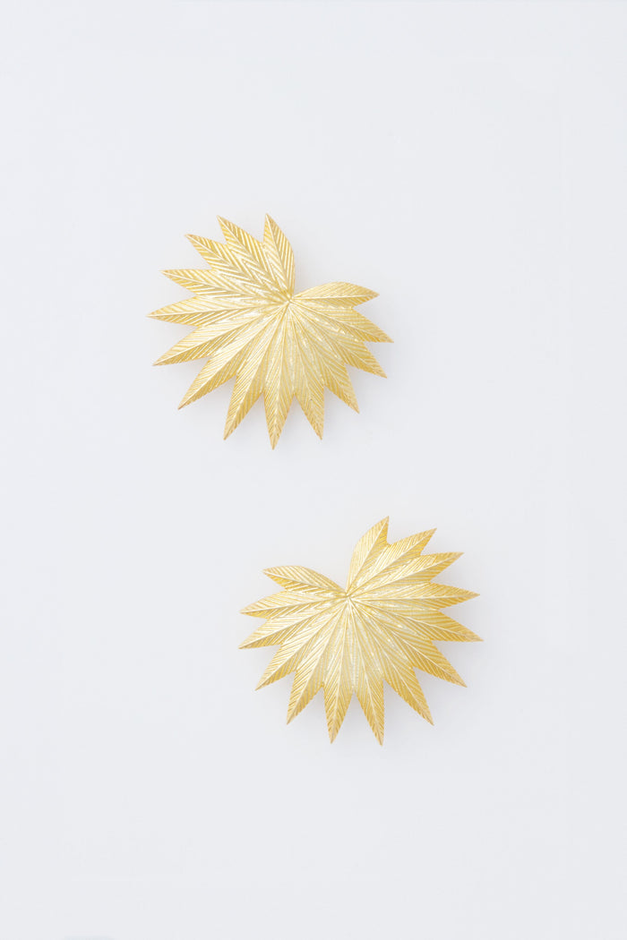 Modafleur’s gold, starburst-shaped Palm Earrings with textured lines are displayed, creating a striking accent for bold outfits and gold plated jewelry collections.