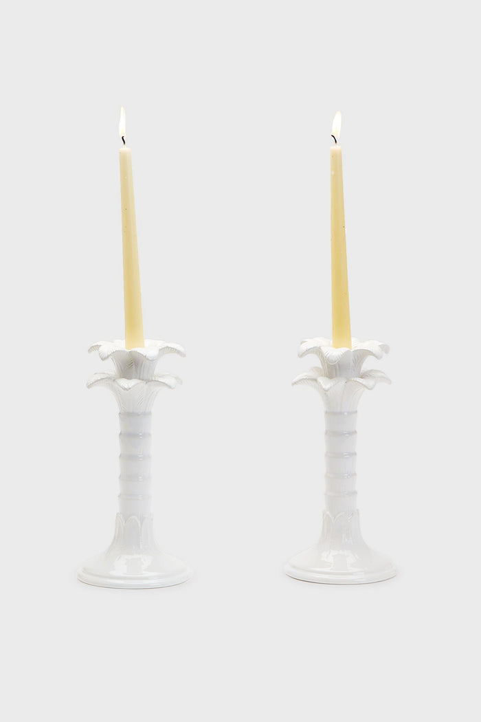 Two lit cream-colored candles in ornate white ceramic candlestick holders by Two's Company, positioned side by side as elegant home decor accents.