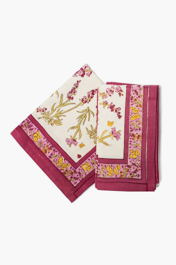 Two folded Couleur Nature Paris handmade napkins with a cream base, botanical yellow and pink floral print, and a magenta border.