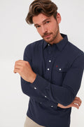 A man with brown hair and a beard wears the Criquet Peacoat Long Sleeve Players Shirt, a stylish men's performance shirt with white buttons, paired with beige pants.