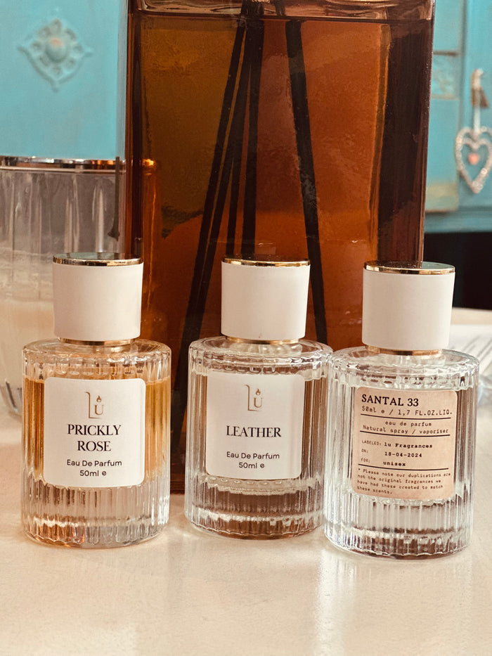 Three perfume bottles labeled 'Prickly Rose', 'Leather', and 'Santal 33' on a reflective surface.