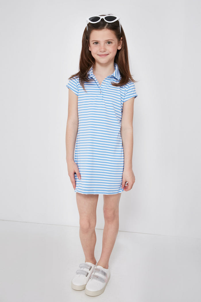 A young girl with brown hair in pigtails wears a Renwick blue and white striped girls' polo dress made from performance fabric, paired with white sneakers and white sunglasses on her head.