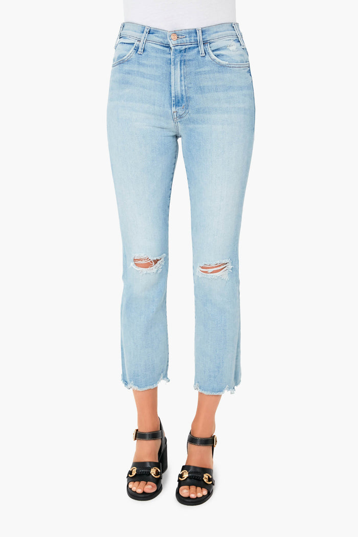 Wearing MOTHER light blue, high-waisted stretch denim cropped jeans with knee rips and frayed hems, paired with black heeled sandals featuring gold accents.