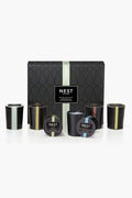 A NEST New York mini votive set with six black candles in glass holders, each featuring a different colored stripe and label, displayed in front of the box.