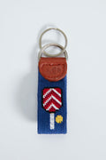 This Smathers and Branson needlepoint key fob features a blue strap, red and white paddle design with a yellow dot, brown leather accent stamped with "S&B," and a metal keyring—an ideal pickleball accessory.