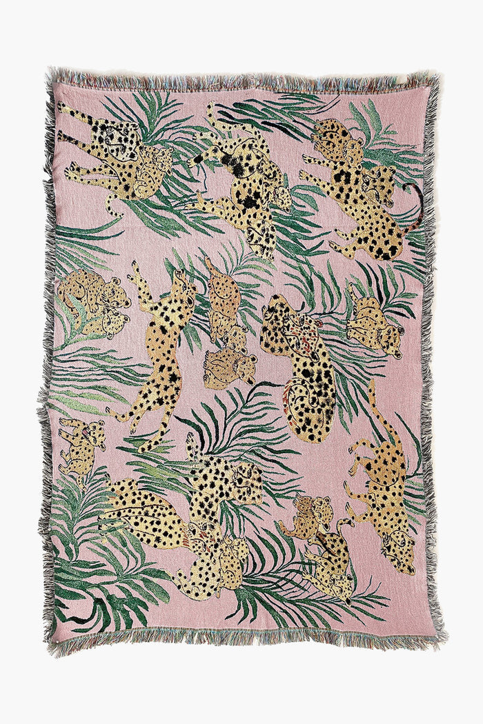The Olivia Wendel Pink Cheetahs Blanket features spotted leopards and green leaves on a pink background, finished with a fringe. Made from 100% US-grown cotton, it adds a playful accent to any room.