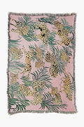 The Olivia Wendel Pink Cheetahs Blanket features spotted leopards and green leaves on a pink background, finished with a fringe. Made from 100% US-grown cotton, it adds a playful accent to any room.