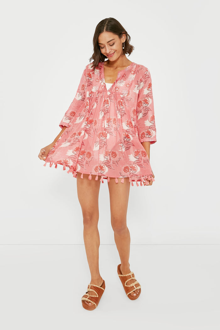 A woman in a pink floral tassel tunic dress by Ro's Garden, styled with brown sandals, holds the sides of her boho-chic cover-up—an ideal vacation-ready look for your next getaway.