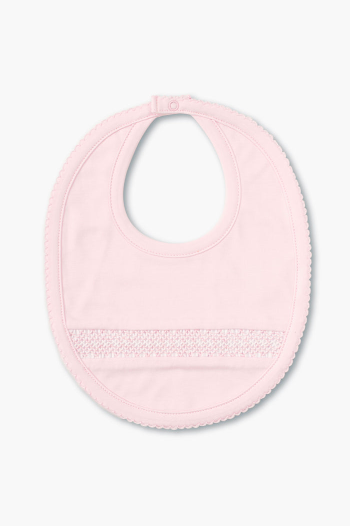 The kissy kissy light pink hand-smocked baby bib features a snap closure, delicate front detailing, and is crafted from soft pima cotton.