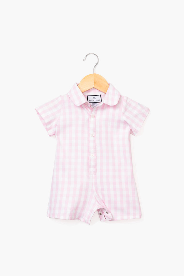 A Petite Plume short-sleeve Pink Infant Gingham Romper with a collar and front buttons, made from luxury cotton sleepwear, is displayed on a wooden hanger.