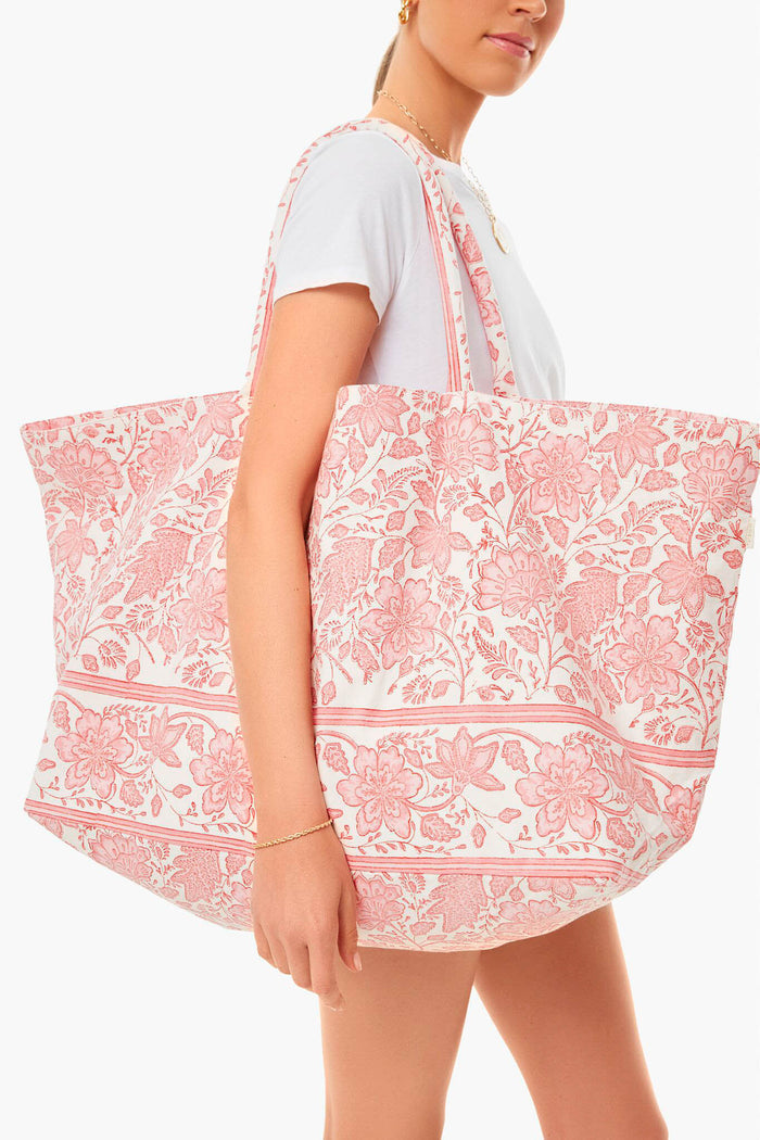 A woman in a white t-shirt carries an oversized Bell by Alicia Bell hand block-printed tote with a pink floral pattern, perfect for resort wear.