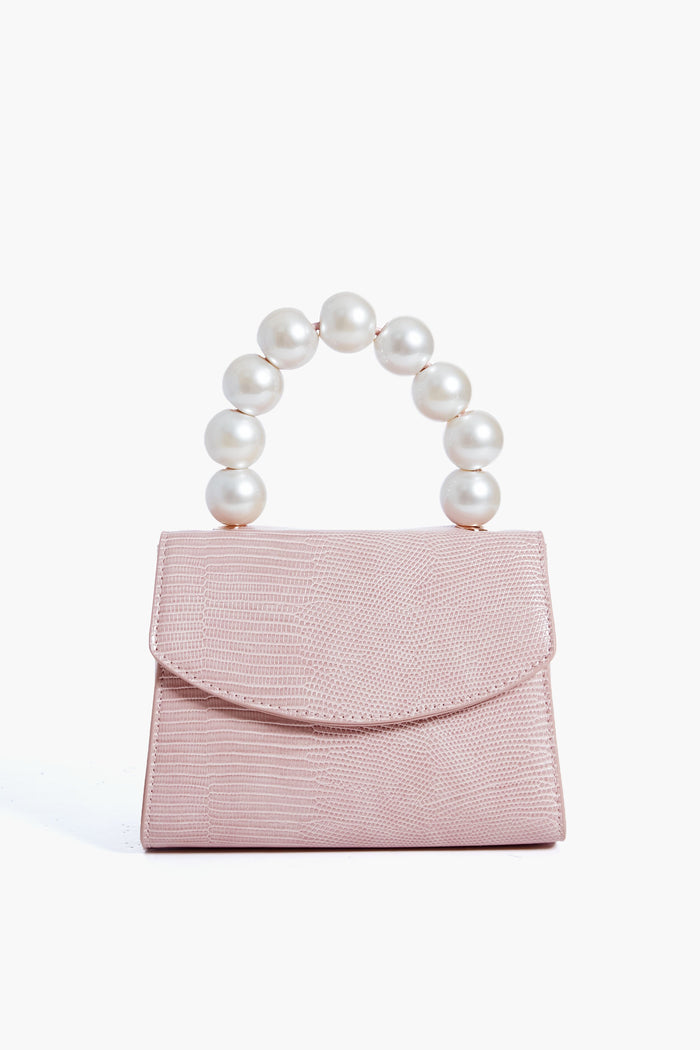 The Olga Berg evening bag is small and pale pink, crafted from textured faux leather, featuring a flap closure and a handle made of large white pearls.