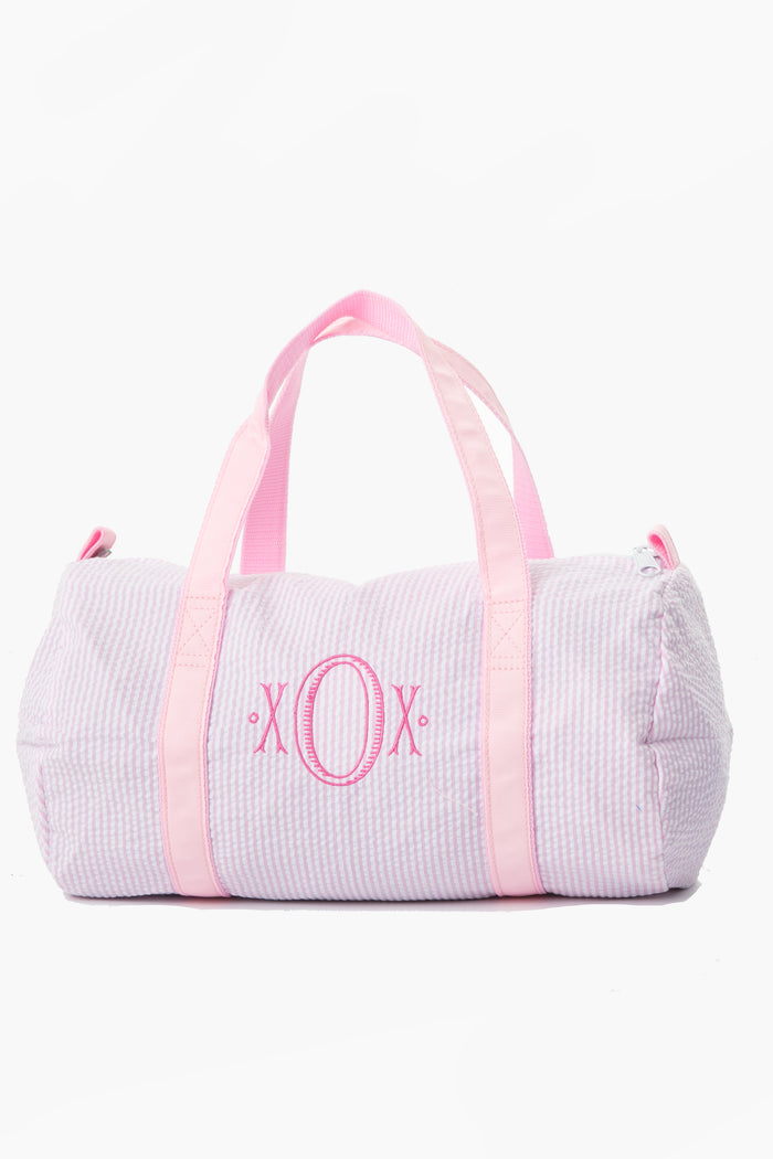 A light pink and white striped Caton's Wharf overnight bag with pink handles and a pink "XO" embroidered monogram on the front.