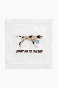 An August Morgan white cocktail napkin features an embroidered brown and white dog with a blue ball and "POINT ME TO THE BAR" stitched below—perfect for entertaining or as a fun hostess gift.