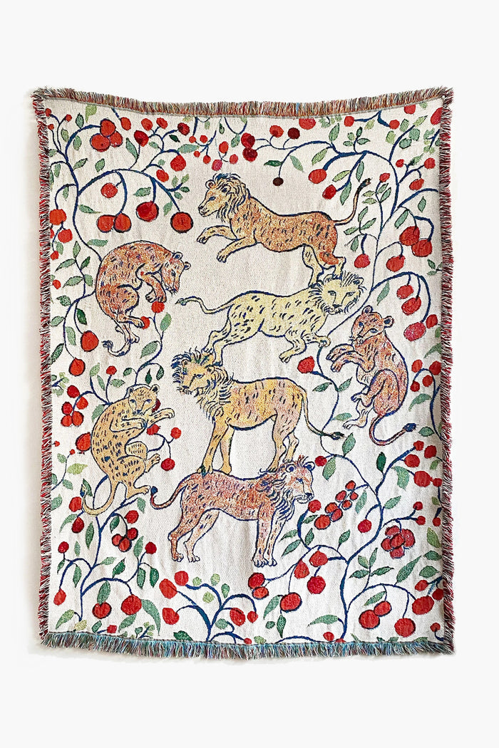 The Olivia Wendel woven throw features six pomegranate lions amid red flowers and green vines, crafted from US-grown cotton and finished with a multicolored fringe.