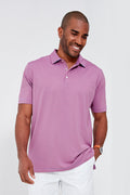 A man in a Peter Millar light purple moisture-wicking performance polo and white pants stands smiling as he looks down.