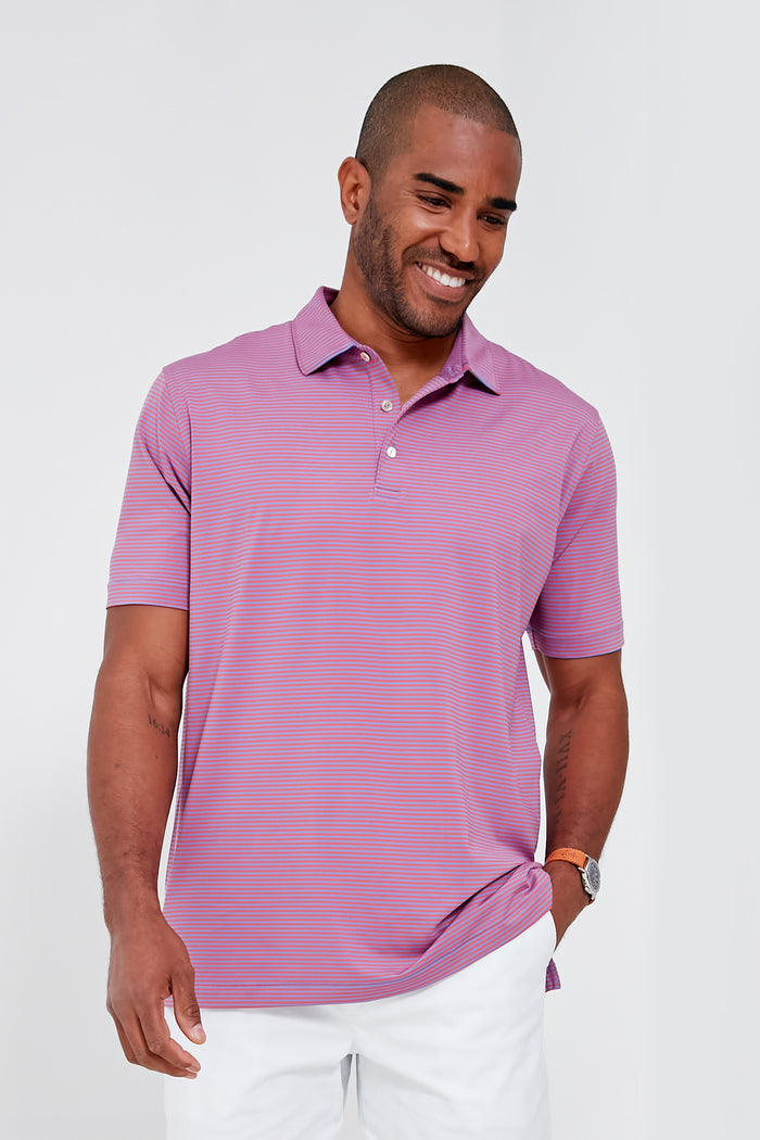 A man in a Peter Millar light purple moisture-wicking performance polo and white pants stands smiling as he looks down.