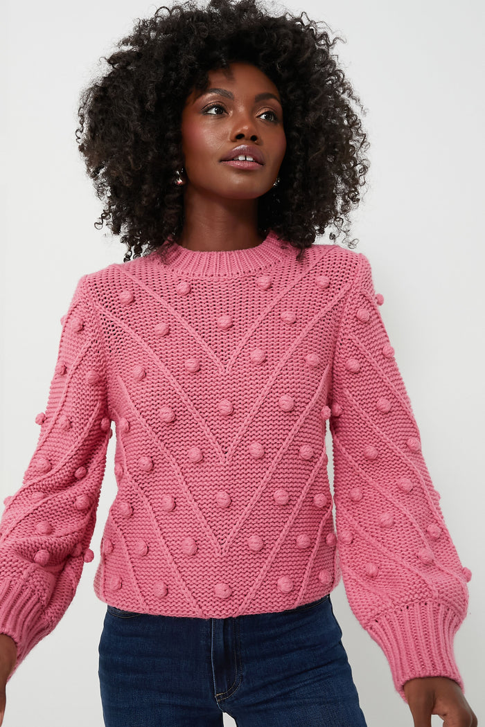 A person wears the Hyacinth House pink pompom sweater with raised bobble details and blue jeans, highlighting the cozy style of this oversized pullover.