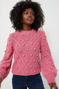 A person wears the Hyacinth House pink pompom sweater with raised bobble details and blue jeans, highlighting the cozy style of this oversized pullover.