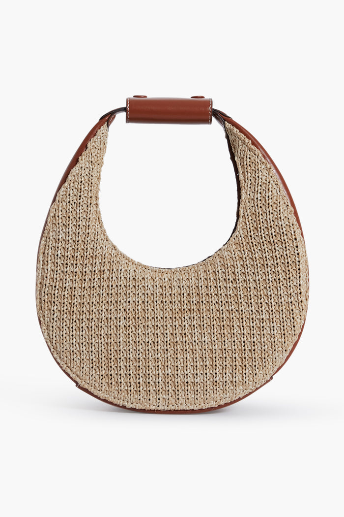 The STAUD Mini Moon Bag features a crescent shape with a woven straw body, brown leather trim, and a structured top leather handle.